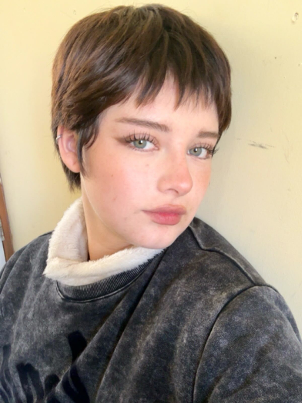 Person poses showing a dark brown pixie cut with wispy, tapered ends