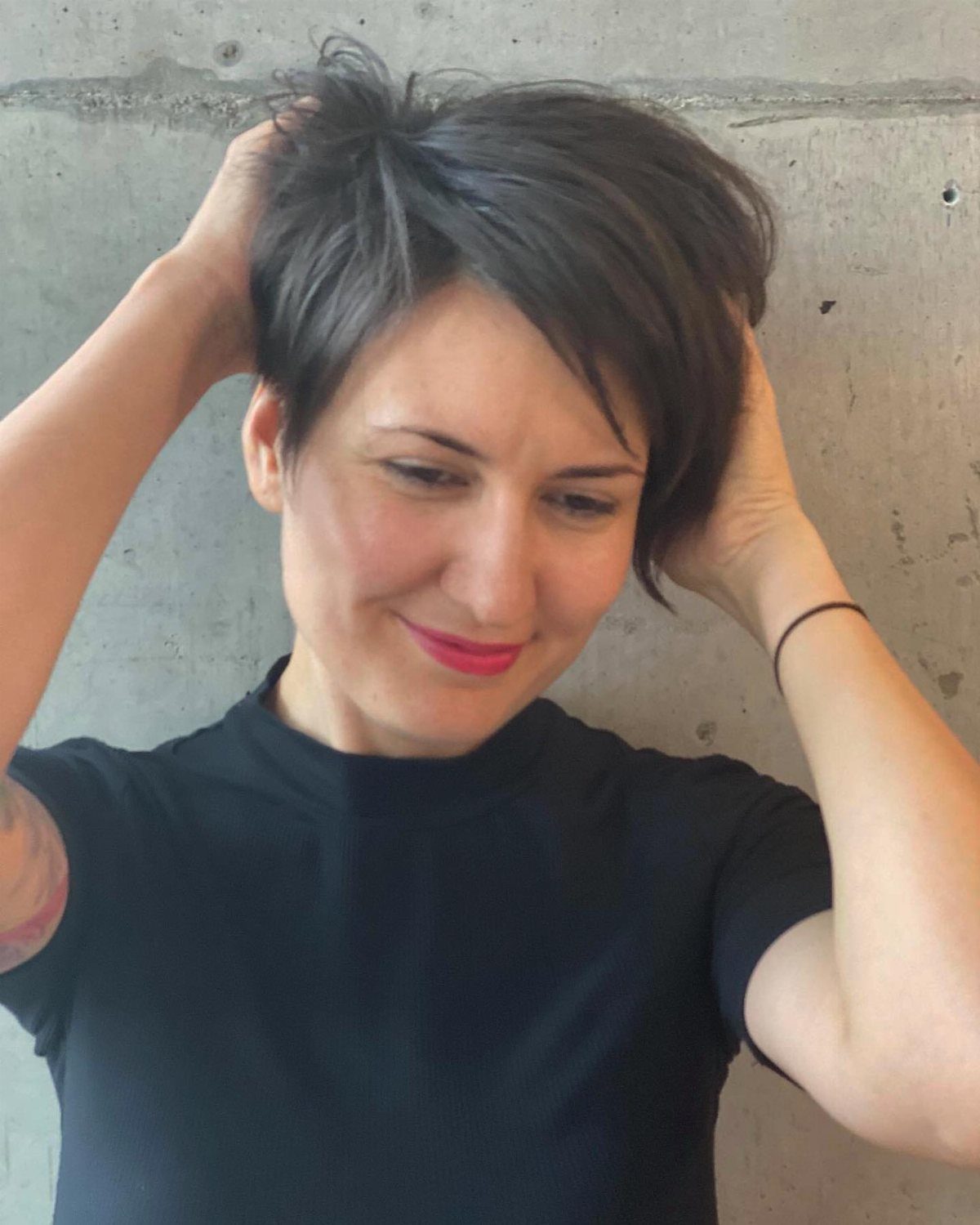 Woman showing a tousled dark brown long pixie haircut against a concrete wall