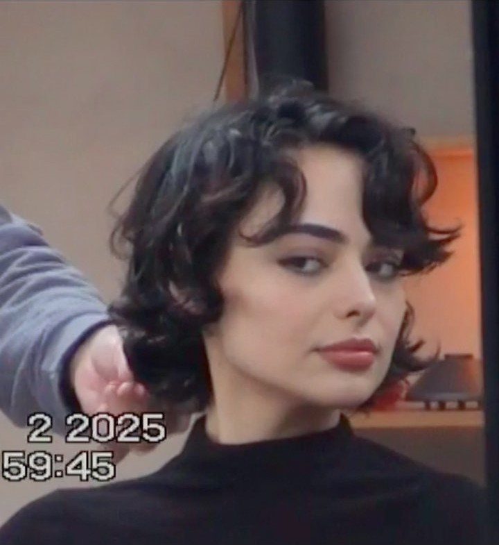 Person with a dark wavy long pixie cut and curls framing the face