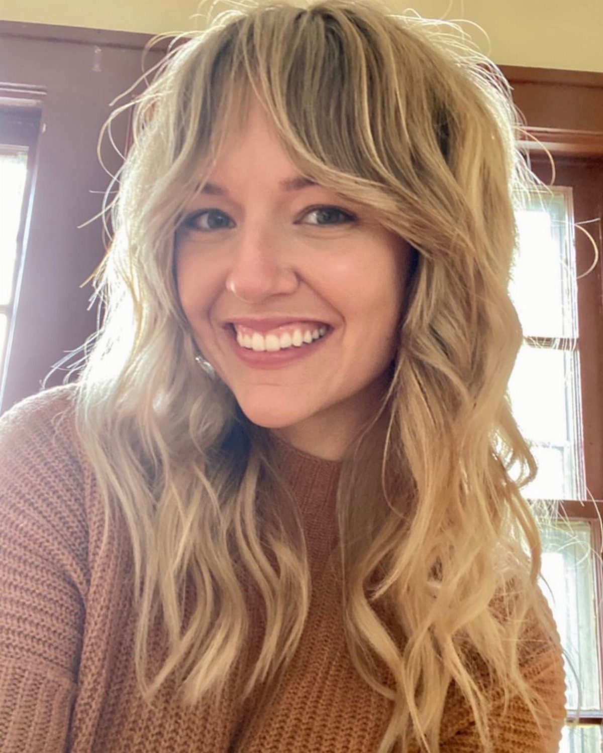 Woman smiling with highlighted blonde layers, long shag, and wispy bangs