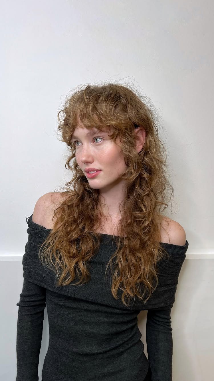 Woman with long layered wavy brown hair and wispy bangs
