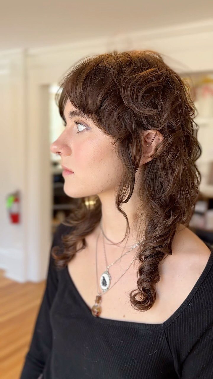 Woman with medium brown curly layers and short bangs in profile