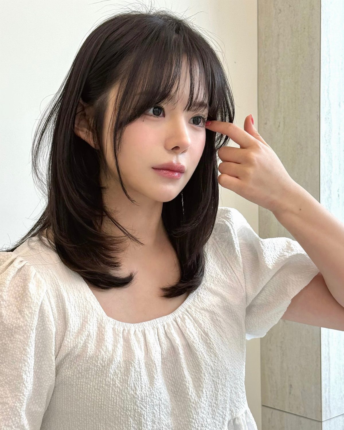 Woman with dark feathered shoulder-length layers and straight wispy bangs
