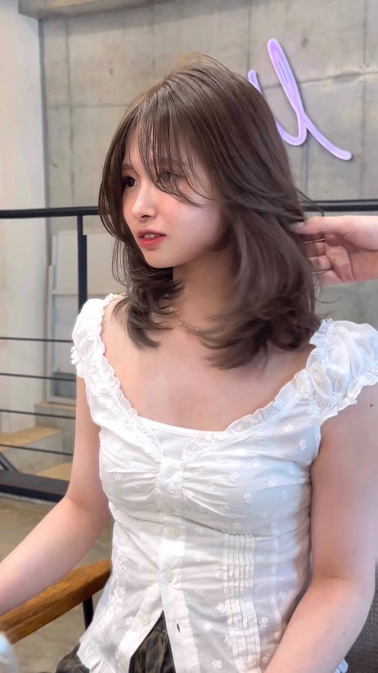 Woman displaying layered brown shoulder-length hair with feathered ends and wispy bangs