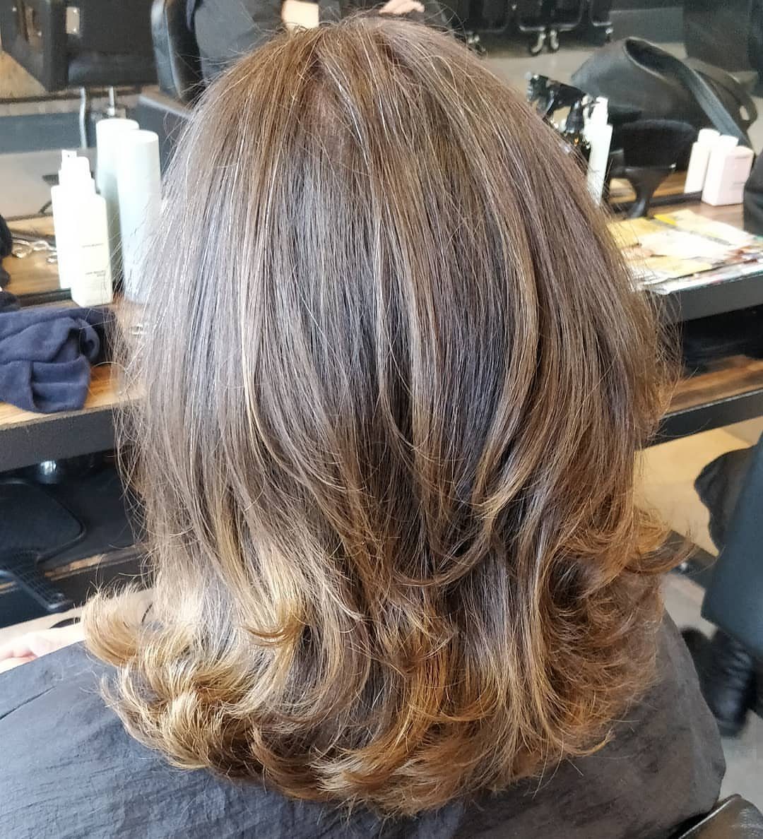 Shoulder-length highlighted brown hair with layered, flipped-out ends in a salon