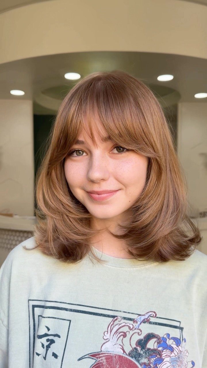 Woman with a copper-brown layered lob, wispy bangs, and curled-under ends