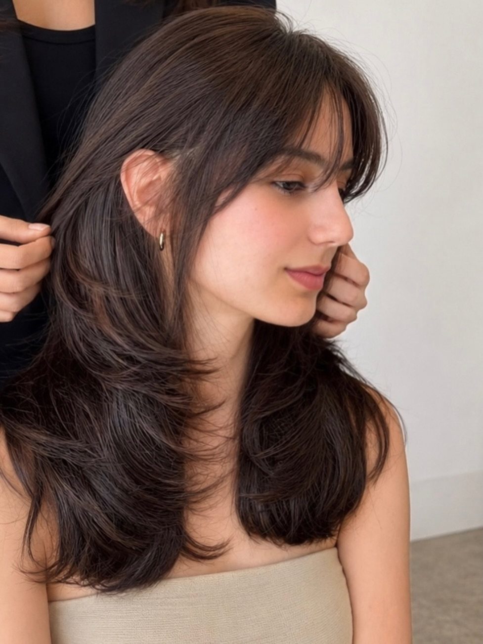 Woman with dark shoulder-length hair showing soft blended layers and wispy bangs