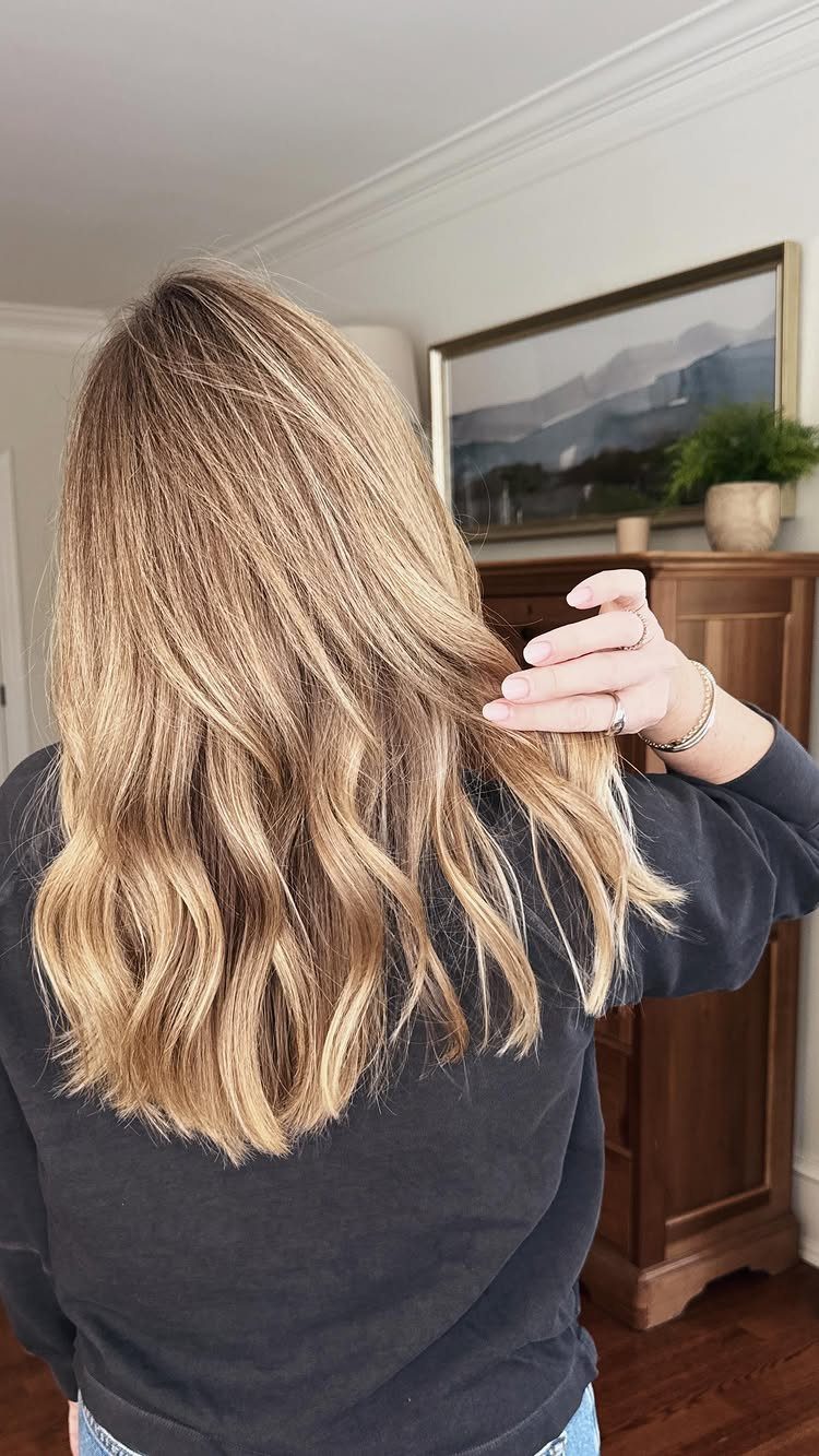 Long blonde layered hair falls in loose waves to the person's mid-back