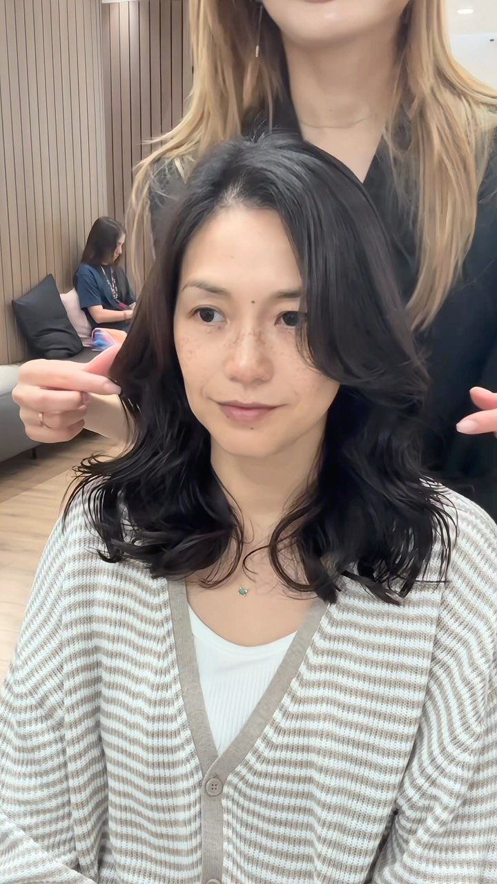 Woman displays shoulder-length dark layered waves while a stylist holds her hair ends