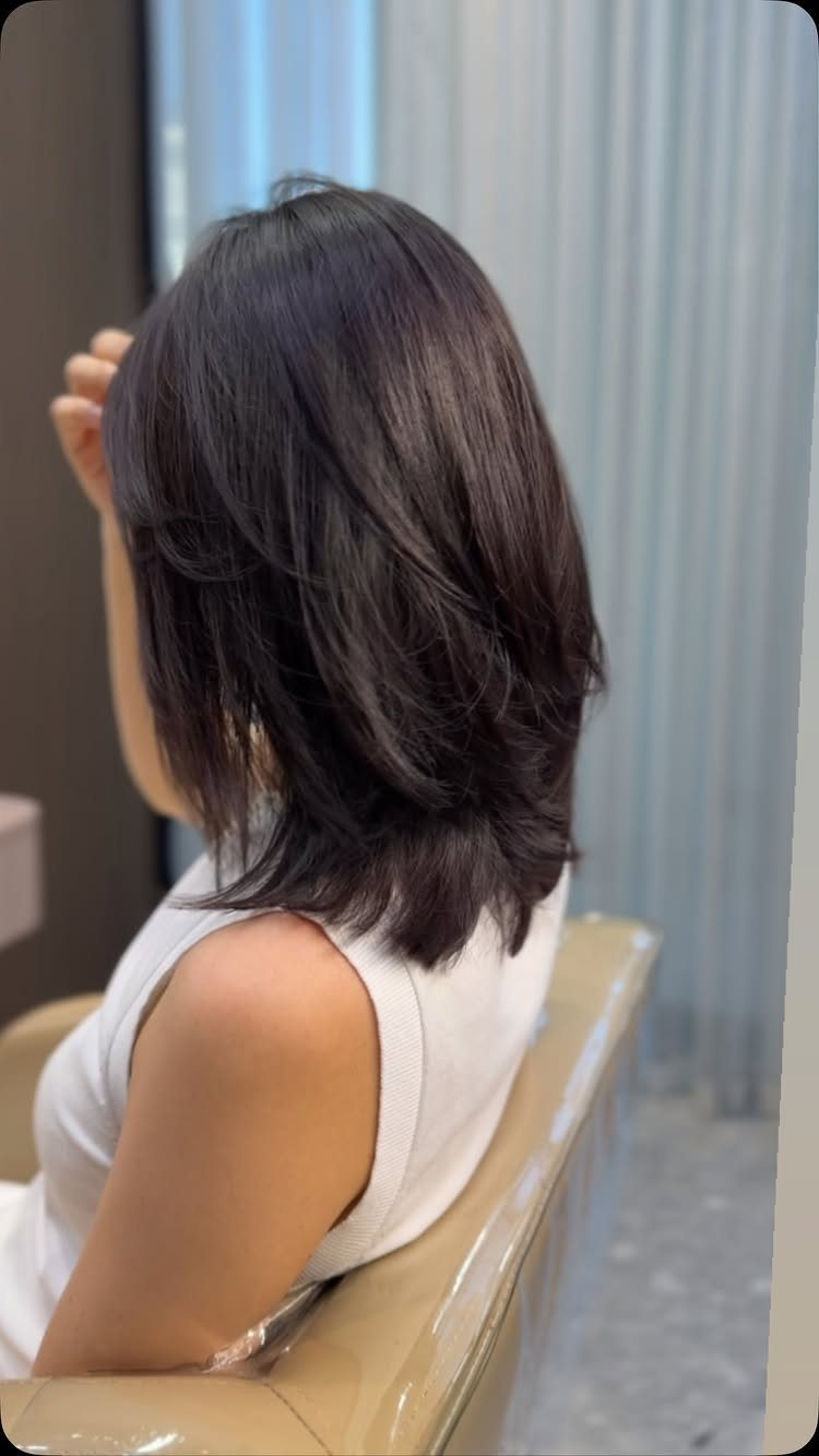 Dark shoulder-length hair with feathered layers throughout, viewed from behind in a salon
