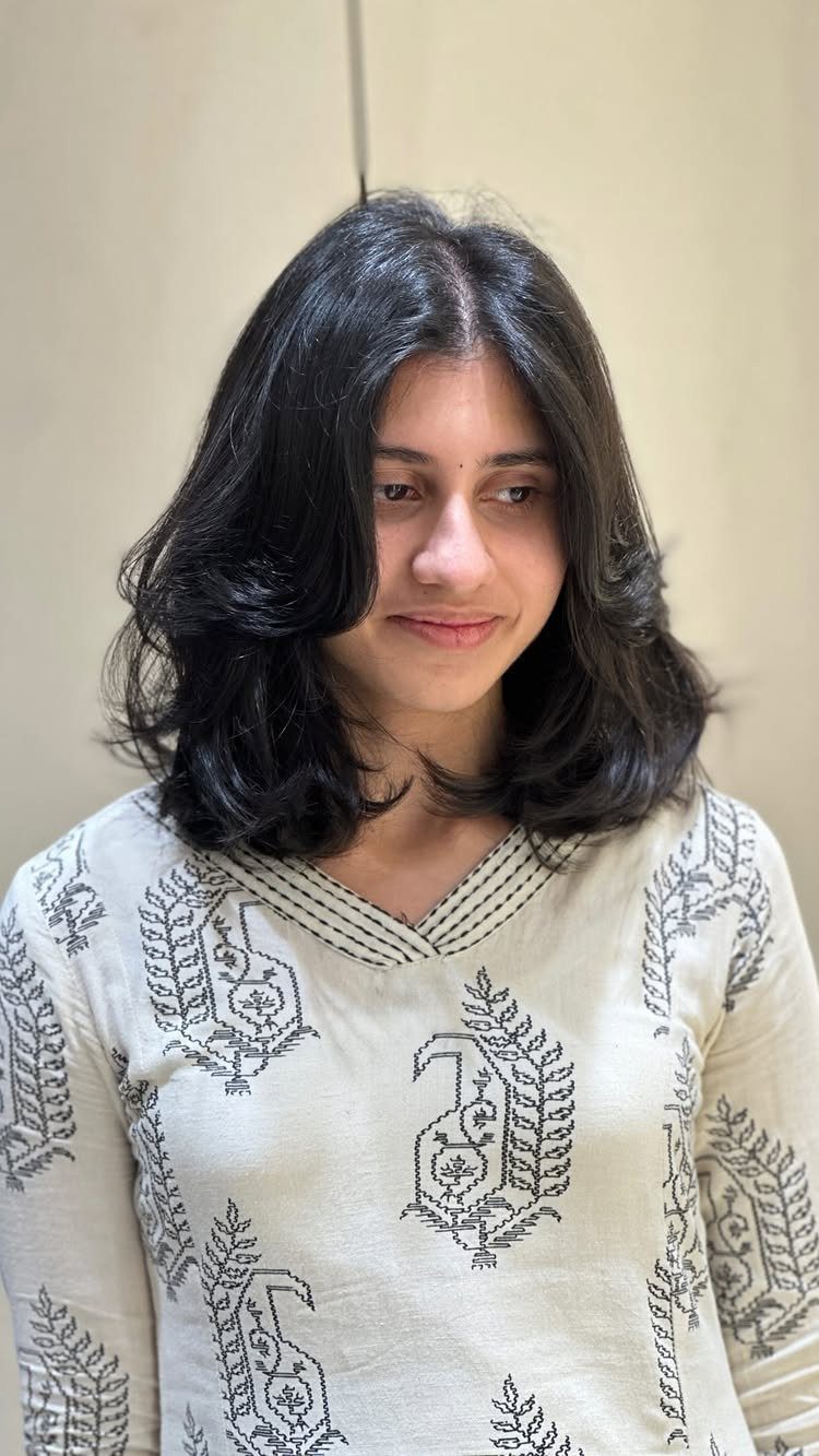 Person with dark shoulder-length hair in a softly layered, wavy lob