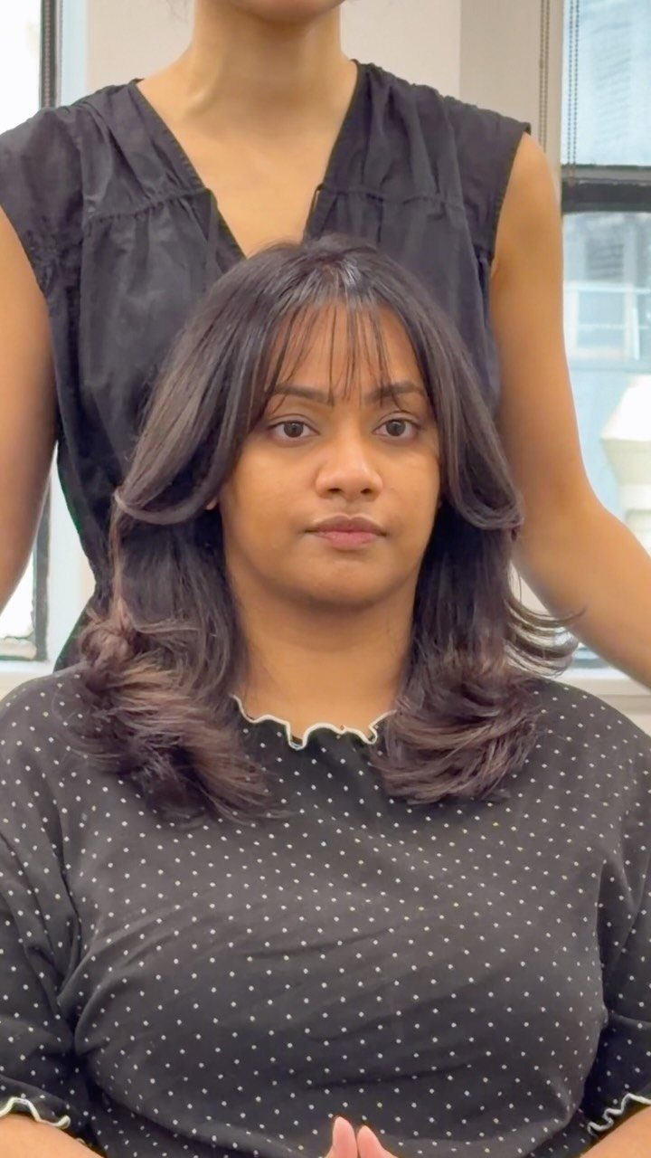 Woman with wispy bangs and medium-length layered hair curled at the ends