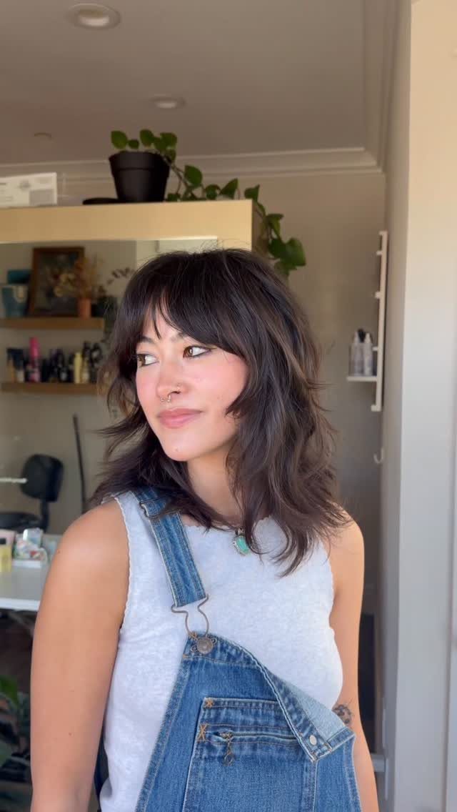 Woman showing a dark, layered midlength shag haircut with bangs