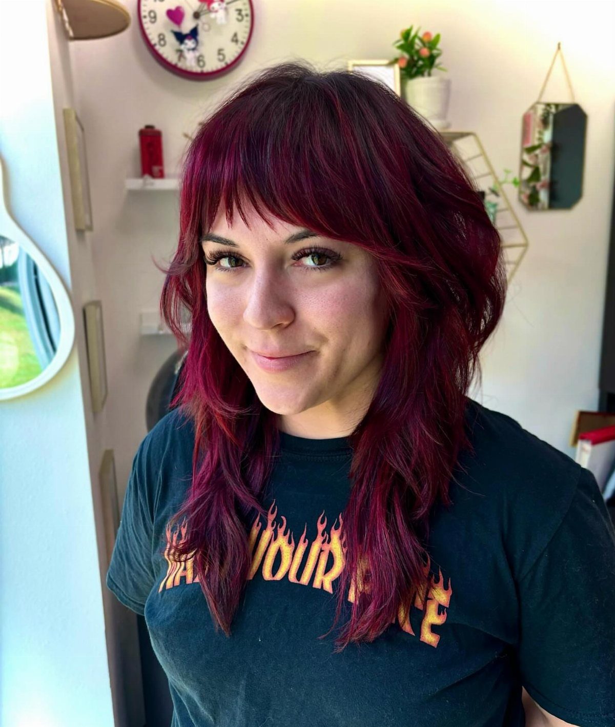 Woman with layered crimson shag haircut, dark roots, and choppy bangs