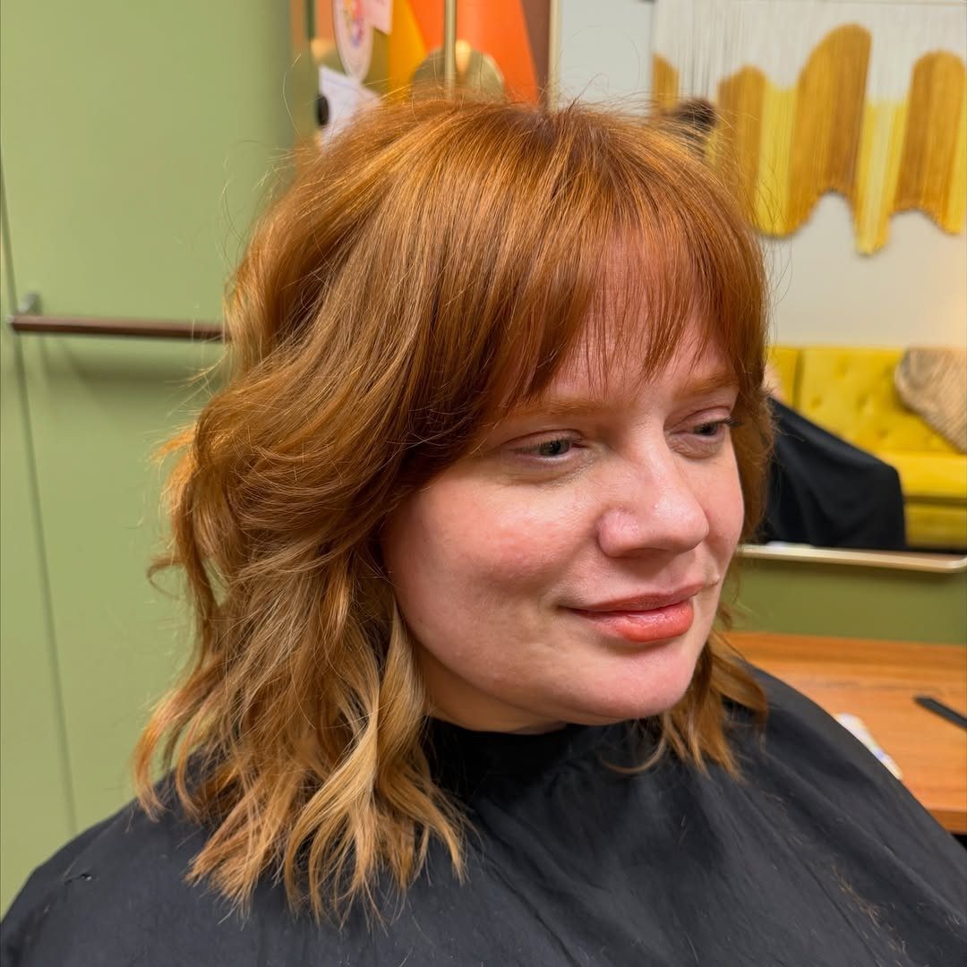 Copper-haired person showing a layered shaggy bob with wispy bangs in a salon