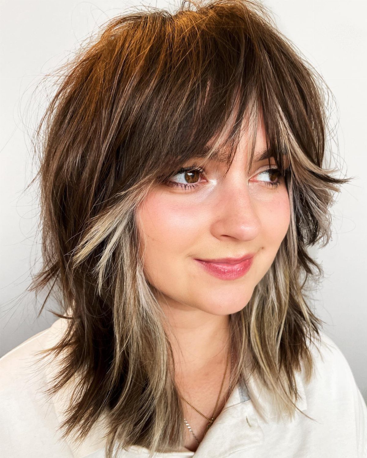 Woman with a tousled brown shag haircut and smoky gray balayage accents