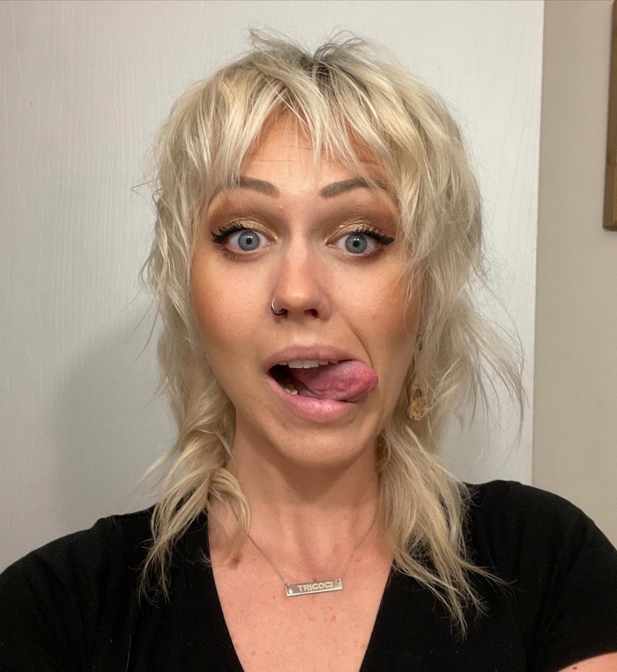 Woman with tousled blonde shag layers and fringe posing against a light wall