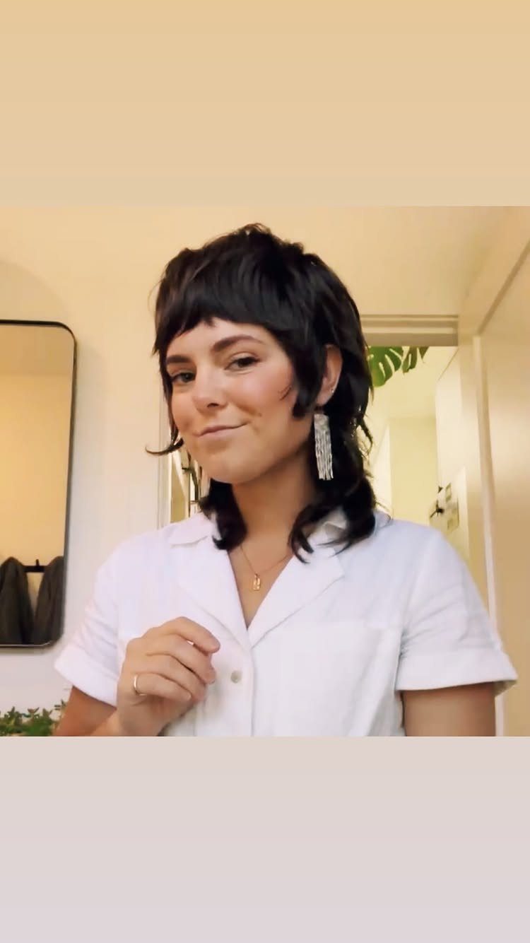 Woman posing with a dark layered midlength haircut and short face-framing fringe