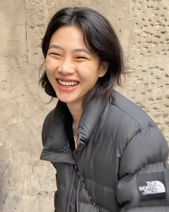 Woman smiling with dark shoulder-length layered haircut against a textured stone wall