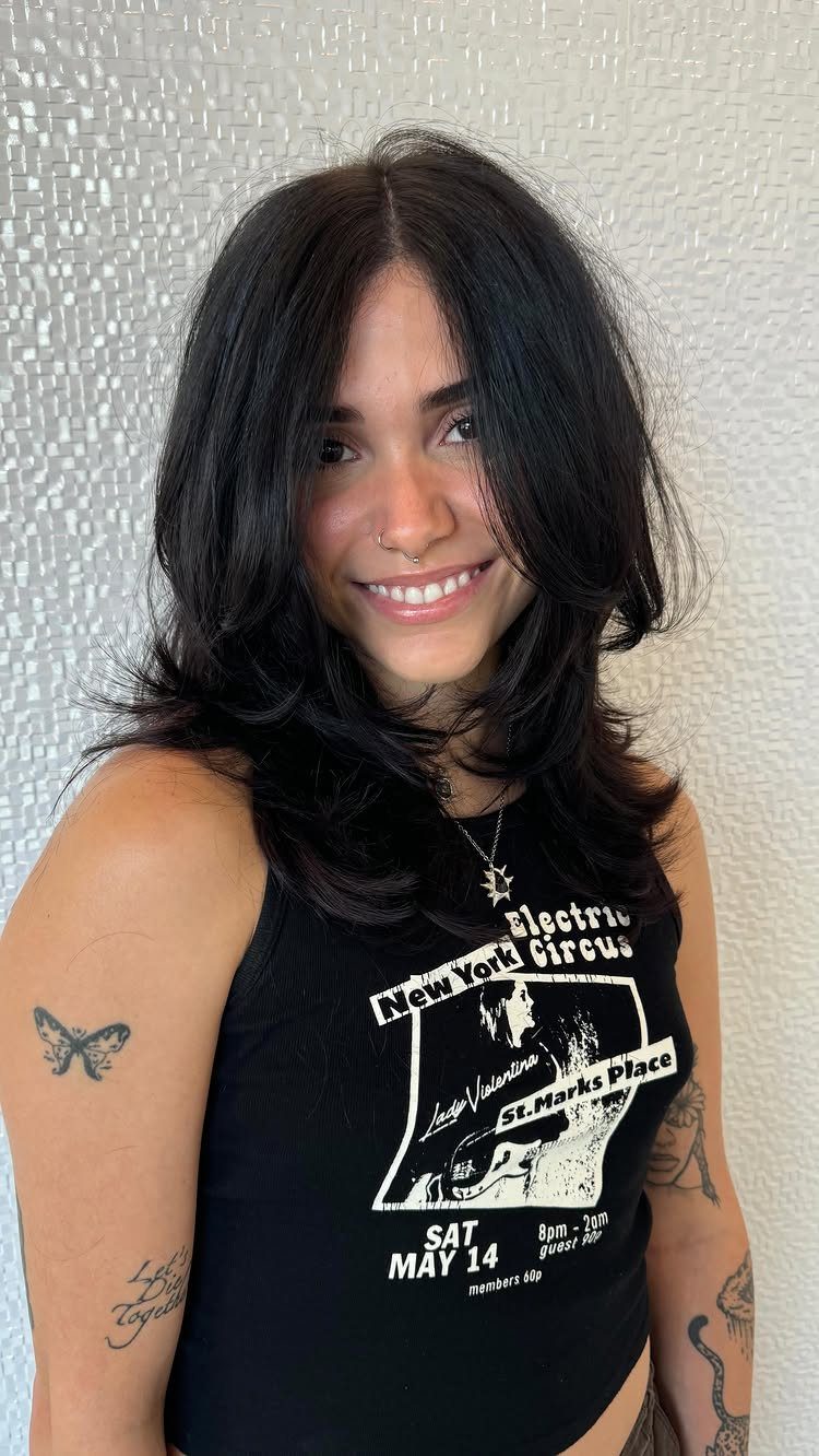 Woman showing dark, shoulder-length hair with layered, softly curled ends