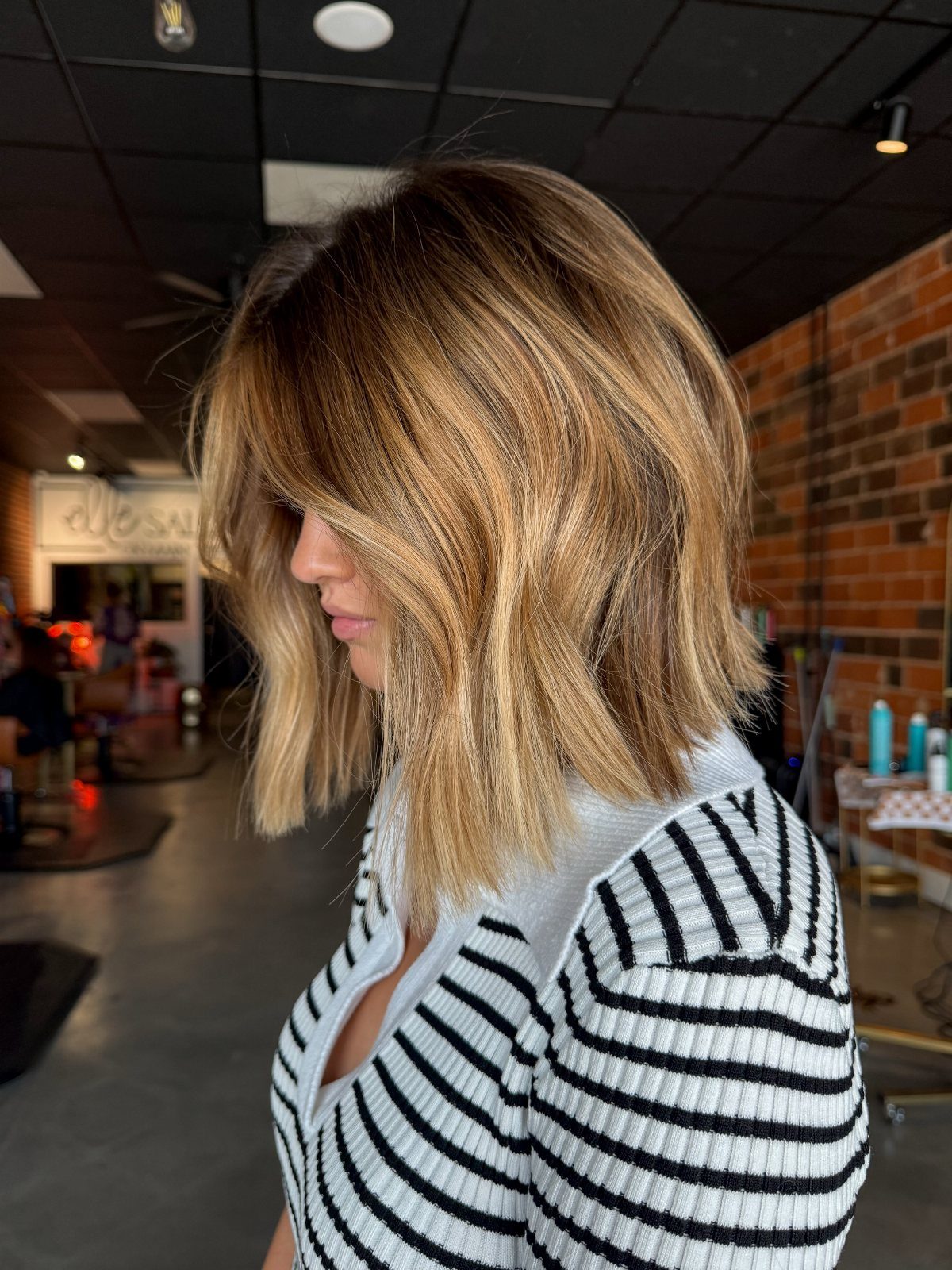 Woman with a tousled blonde bob and dark roots in a salon
