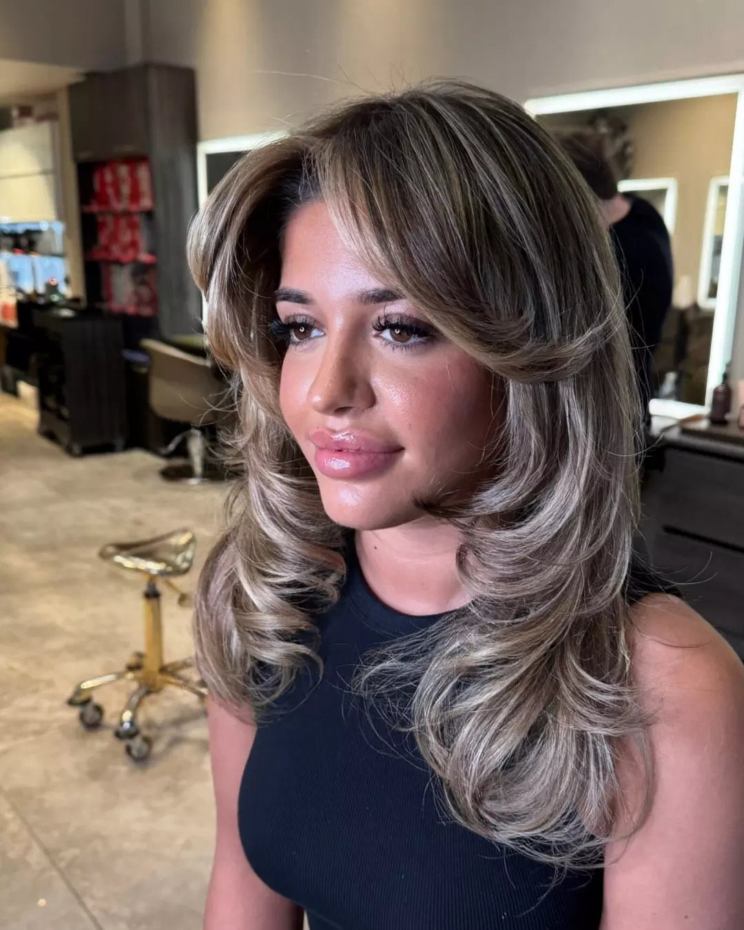 Woman with voluminous layered curls and a deep side part in a salon