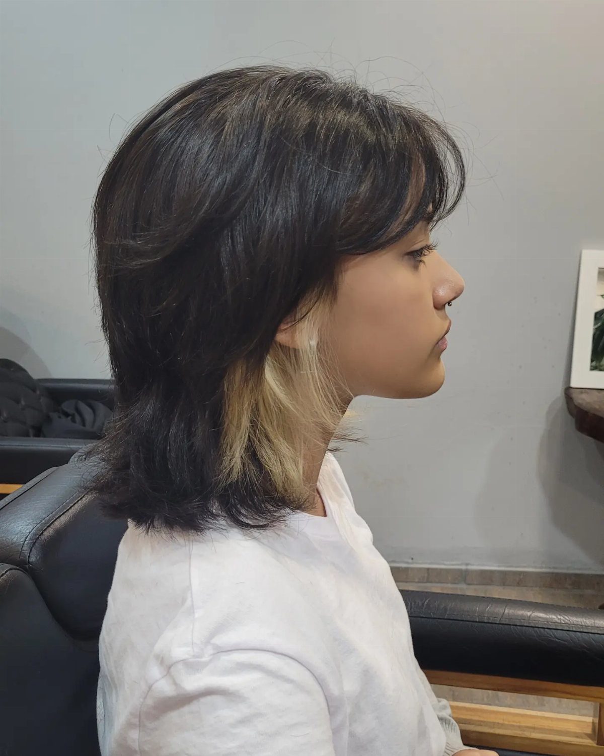 Side-profile person showing a layered dark wolf cut with blonde underlayers