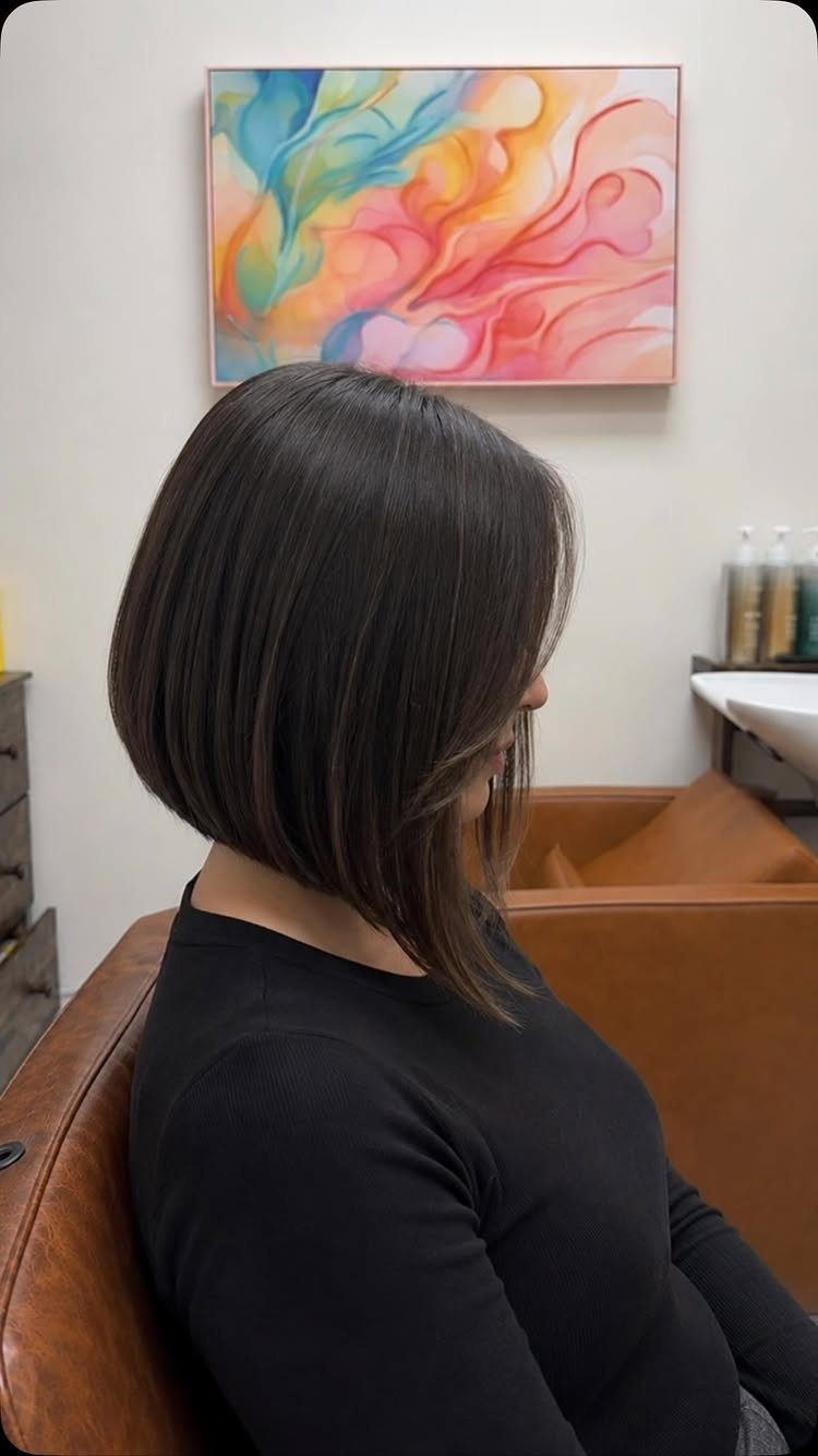 Dark asymmetrical bob with longer face-framing pieces shown in profile at a salon