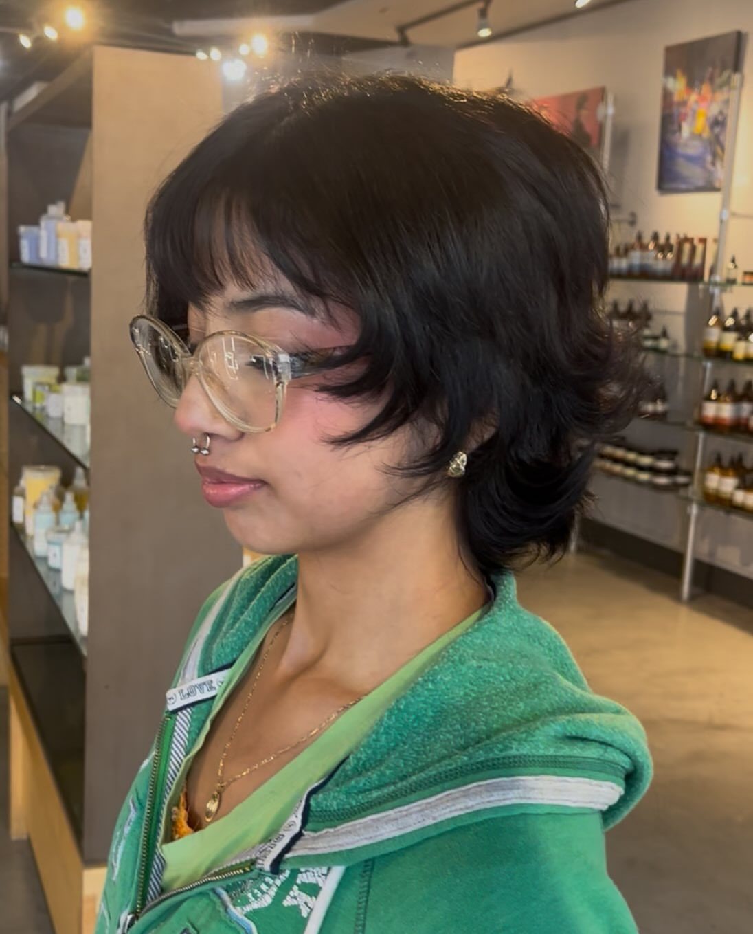 Person with a short, layered dark bixie haircut and wispy bangs in a salon