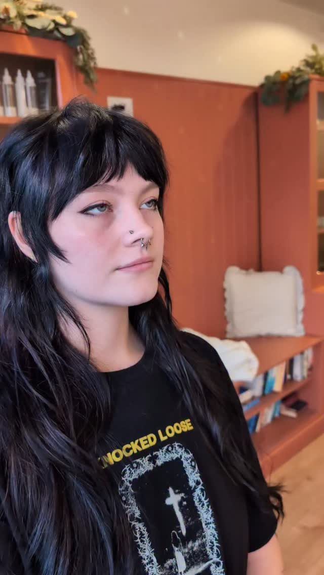 Person with long dark hair, choppy bangs, and face-framing layers in a black T-shirt