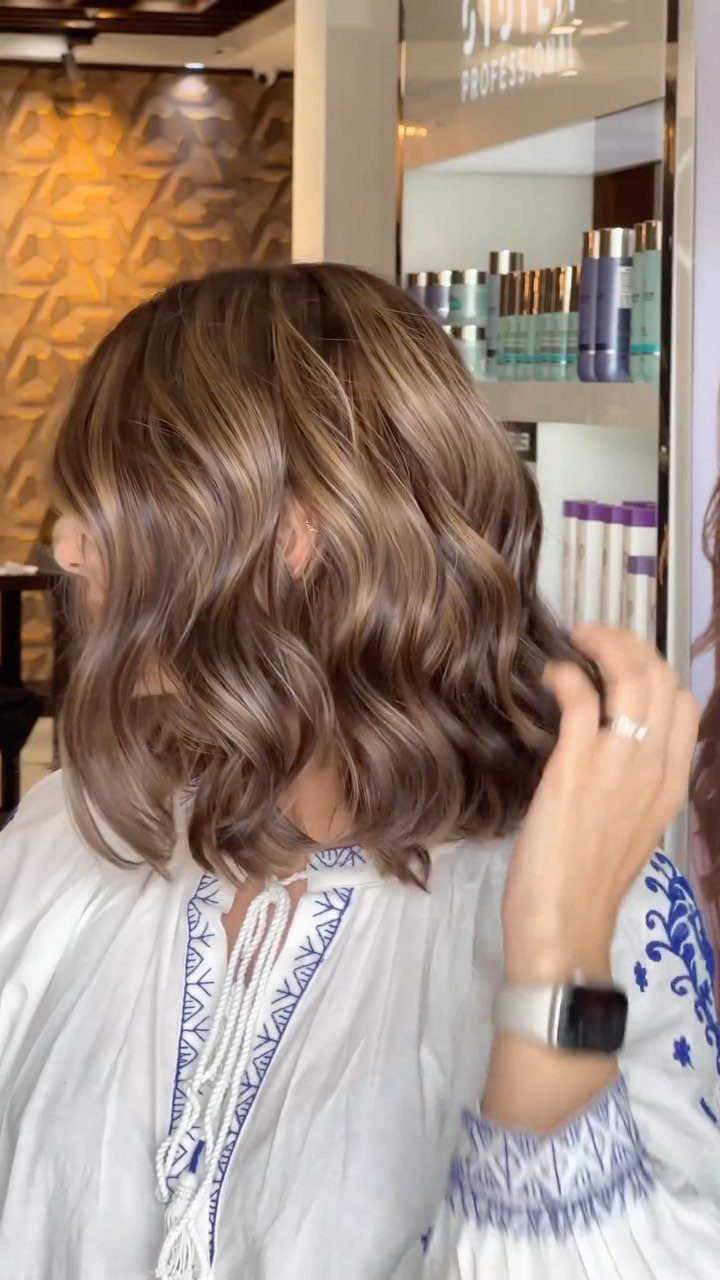 Tousled brown waves with subtle lighter roots shown from behind in a salon