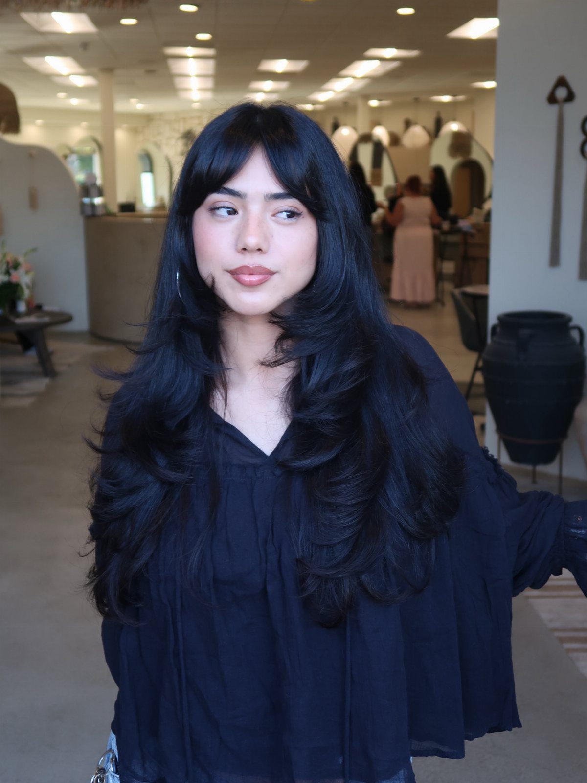 Woman with long dark layered hair and bangs posing in a hair salon