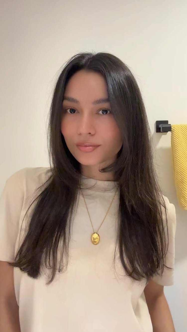 Woman with long dark hair and subtle layers wears a center part