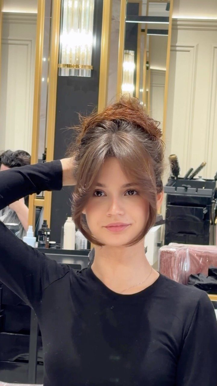 Woman showing a soft updo with loose face-framing layers and bangs in a salon