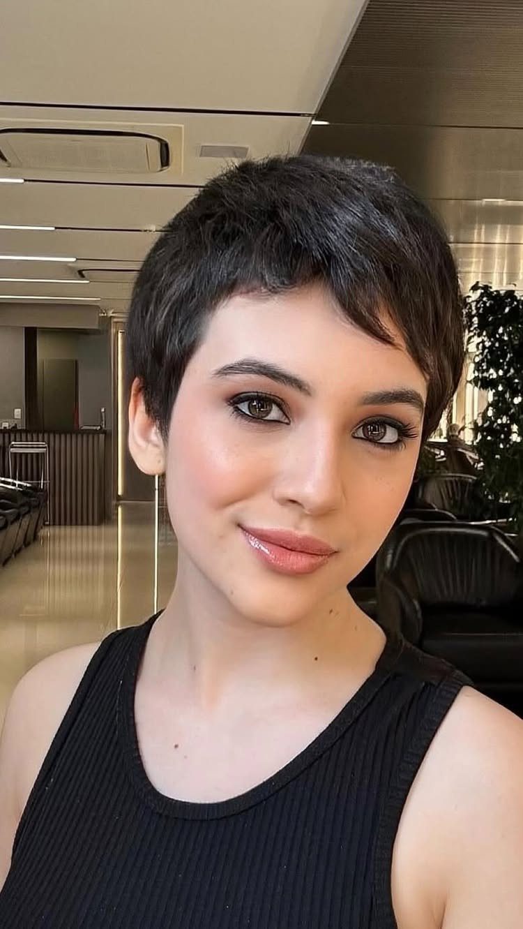 Woman with a short, dark textured pixie haircut posing inside a salon
