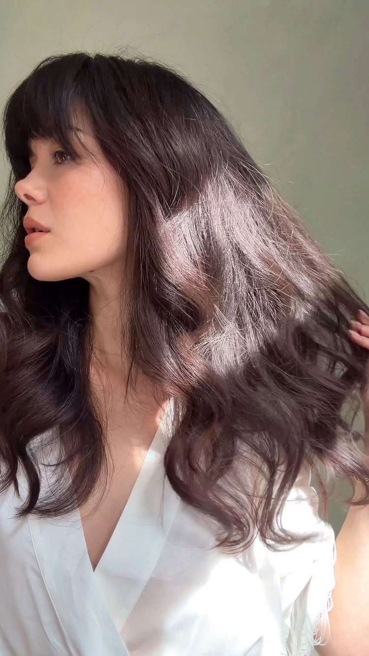 Woman with long dark tousled waves and full bangs, shown in profile