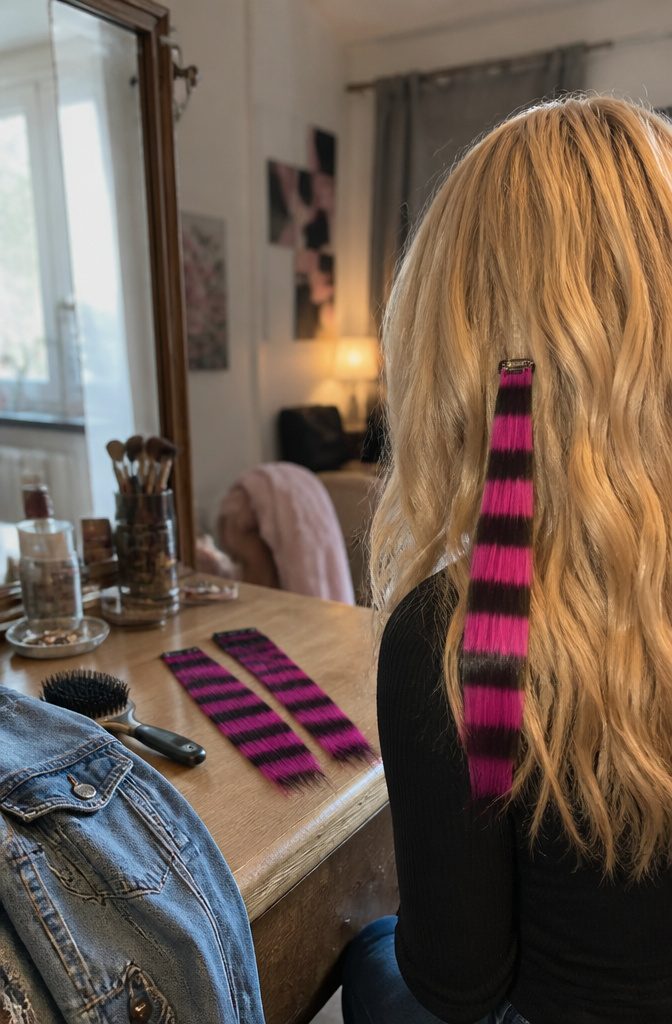 Blonde hair with one pink and black striped extension clipped near the side