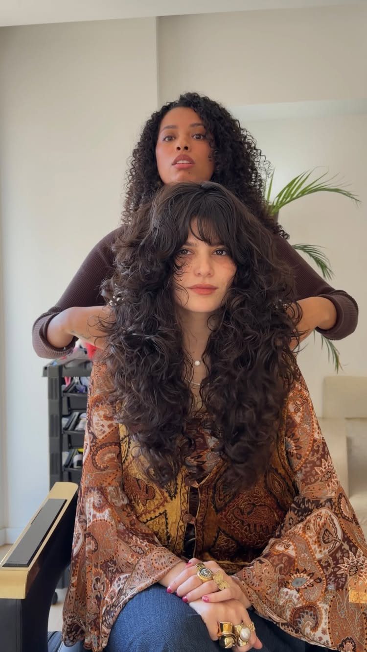 Long curly shag with layered bangs being arranged by a stylist in a salon