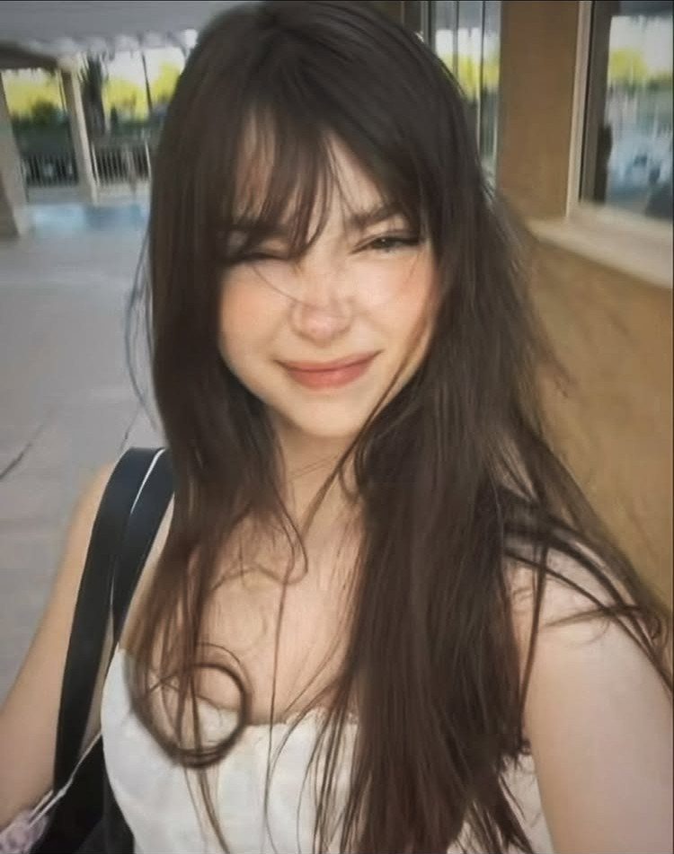 Young woman with long dark hair, wispy face-framing bangs, and a white top