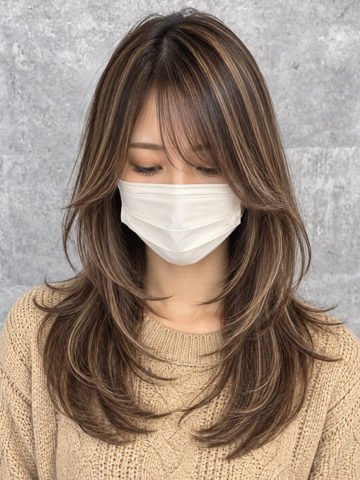 Long brown face-framing layers fall around a masked person’s face