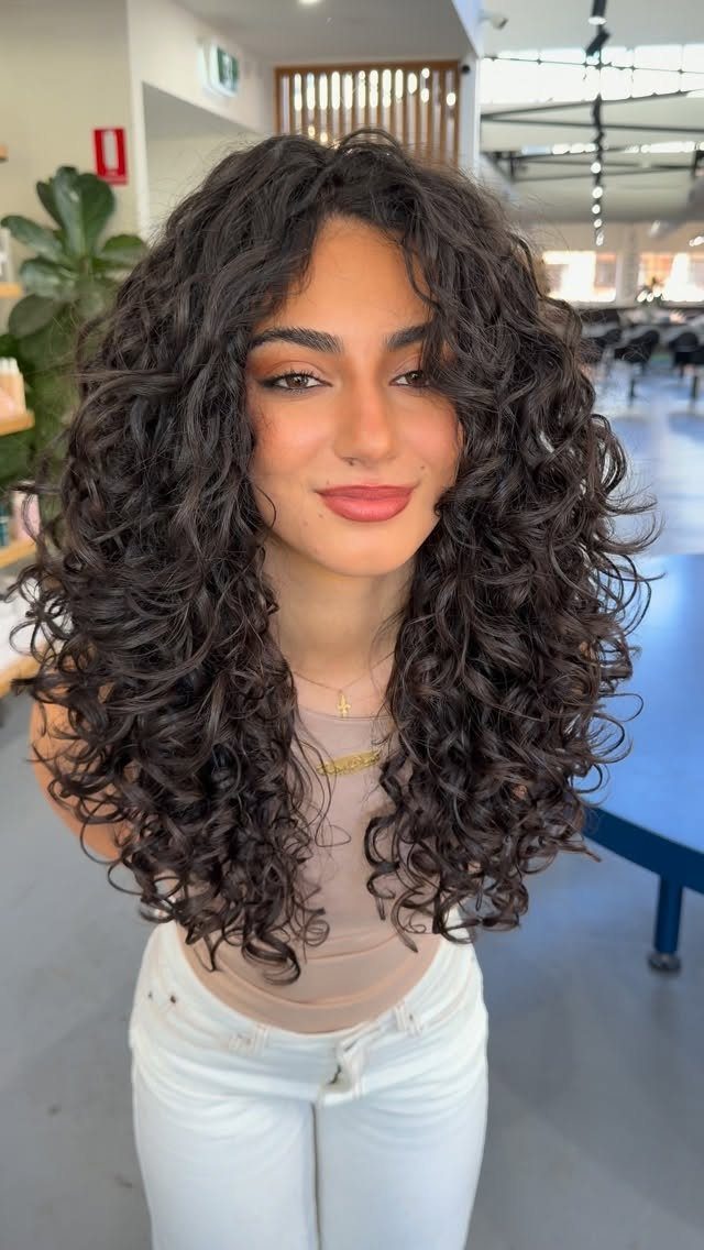 Woman with long dark curls framing her face in a bright salon