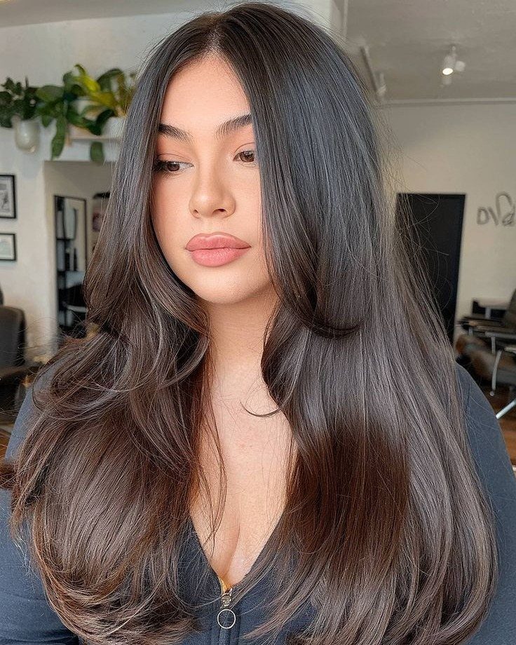 Woman with long, sleek dark hair and face-framing layers in a salon