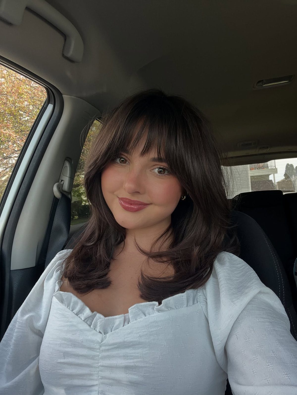Woman with a textured shoulder-length brunette lob and bangs sitting in a car