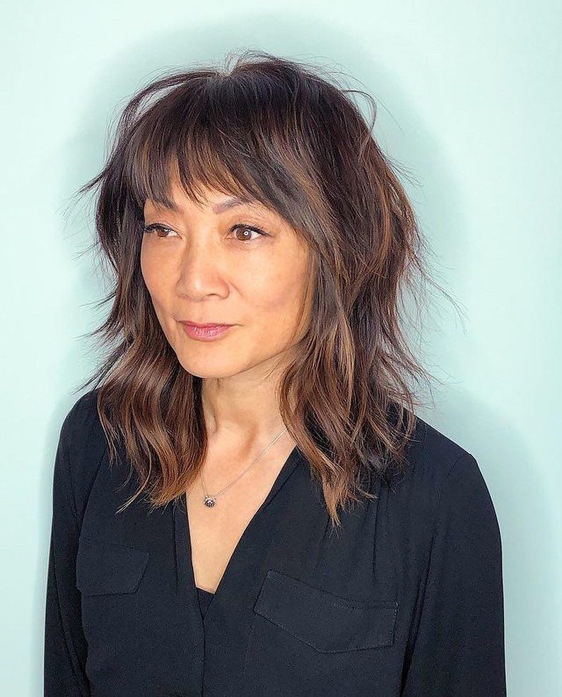 Woman with layered medium-length brown classic shag haircut and wispy bangs