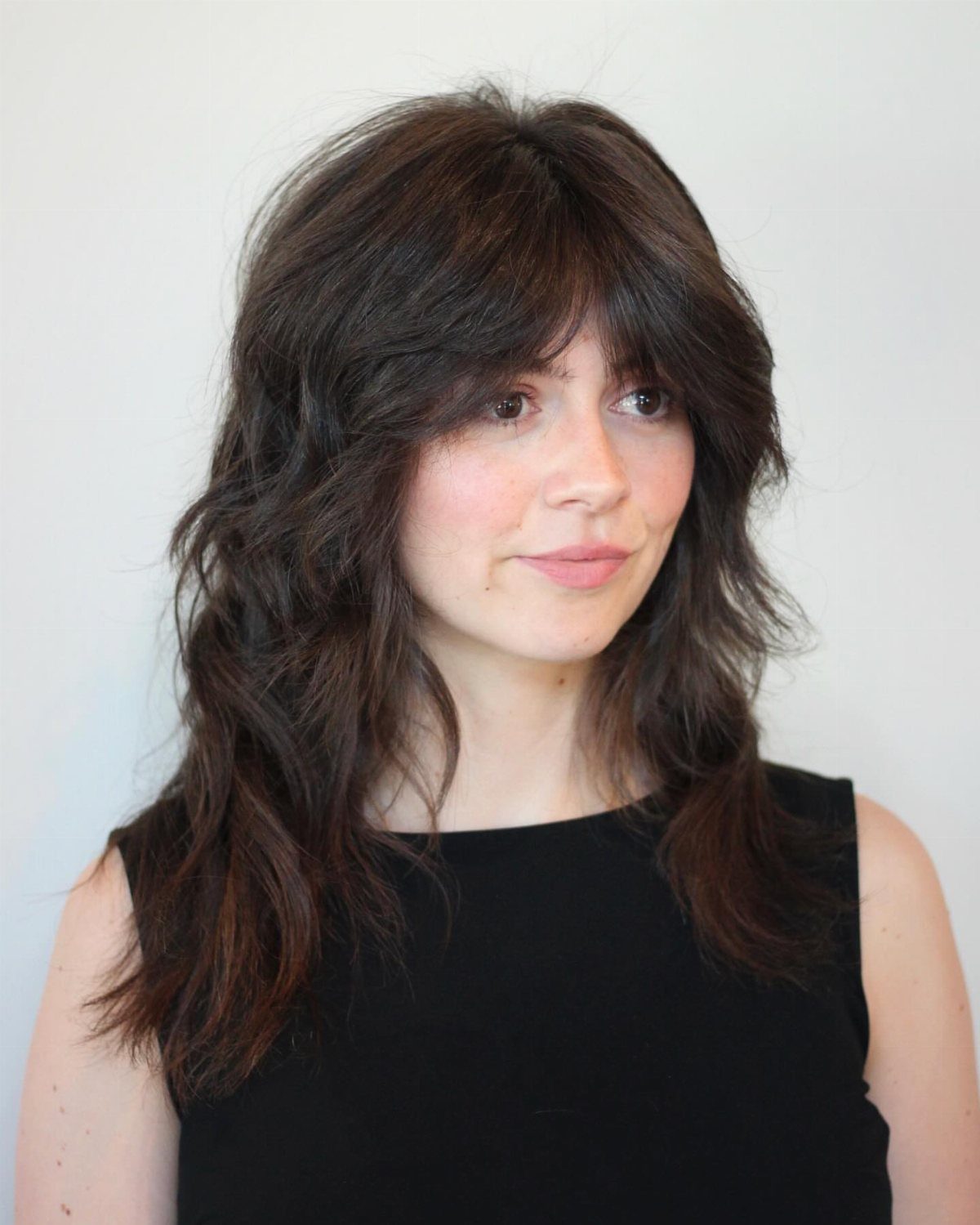 Woman wears a medium-length dark shag with full bangs and textured layers