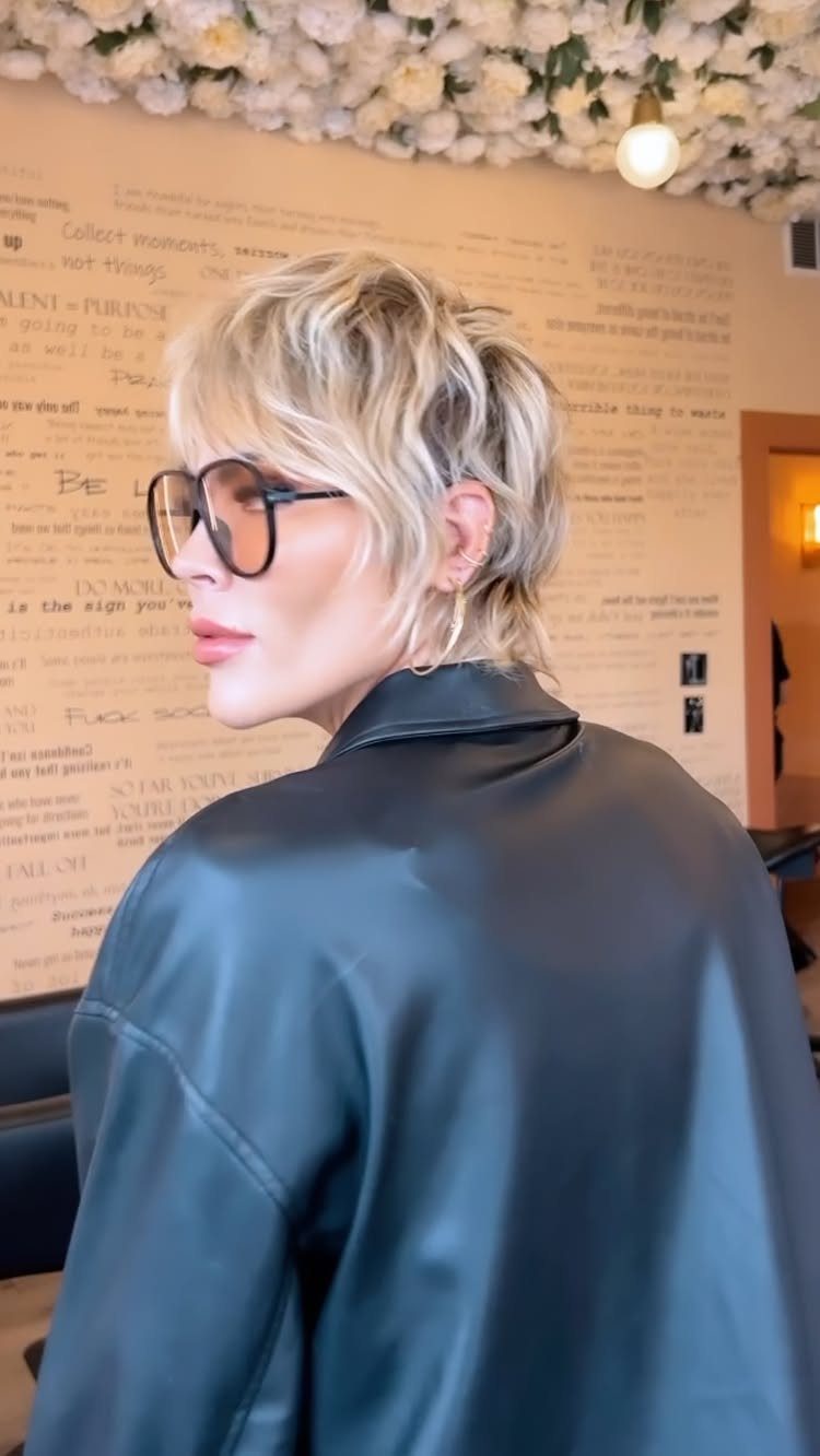Blonde pixie shag haircut with feathered layers and large black glasses