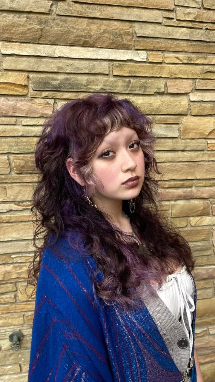 Young woman with layered purple waves and short ringlet fringe against stone