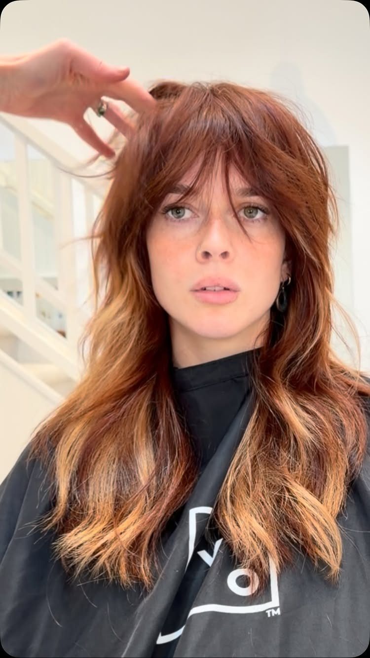 Woman with long, straight auburn shag layers and wispy bangs in a salon