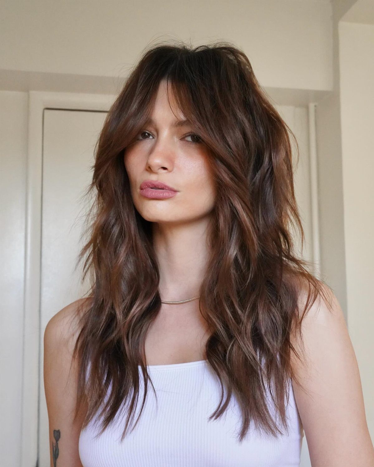 Woman displaying a long chocolate brown shag haircut with layered waves and curtain bangs