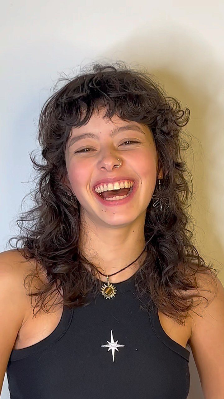 Woman smiling with long dark curls and short, tousled micro bangs